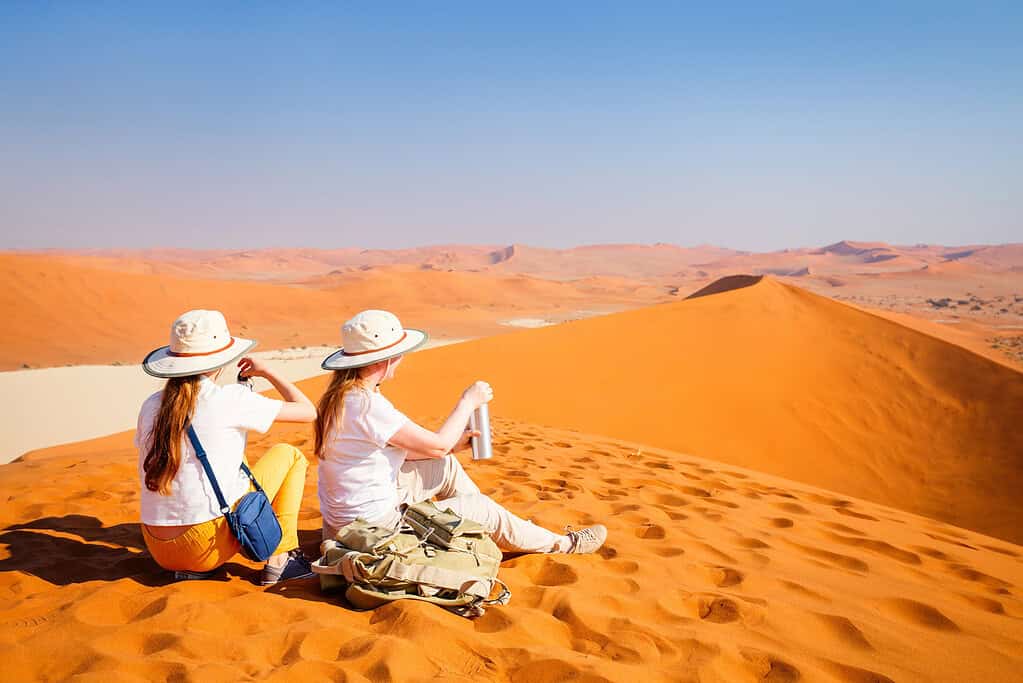Eine Familie mit Mutter und Tochter ruht sich aus, während sie die berühmte rote Sanddüne Big Daddy in Sossusvlei Namibia besteigen